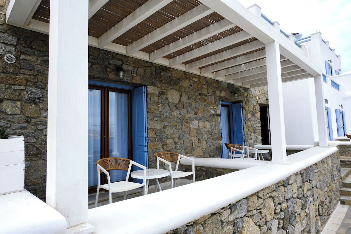 A stone building with white walls and blue doors, featuring outdoor seating with white and wicker chairs.