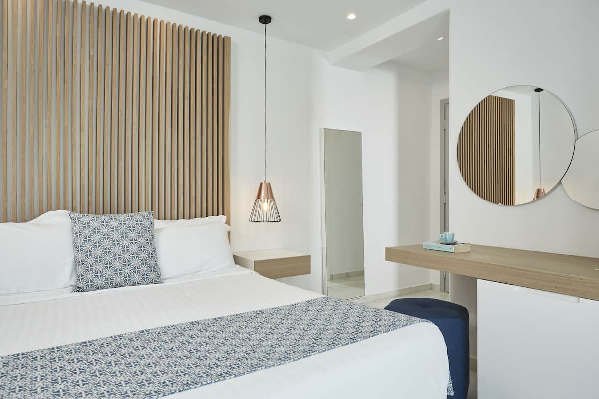 A modern hotel room with a large bed, a bedside table, a desk, a mirror, and a hanging light fixture.