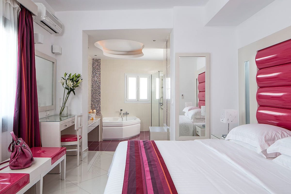 A modern hotel room with a large bed, a vanity with a mirror, a bathtub, and a shower.