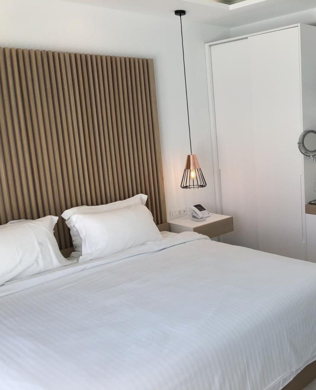 A neatly made bed with white linens, a bedside table with a phone, and a pendant light.