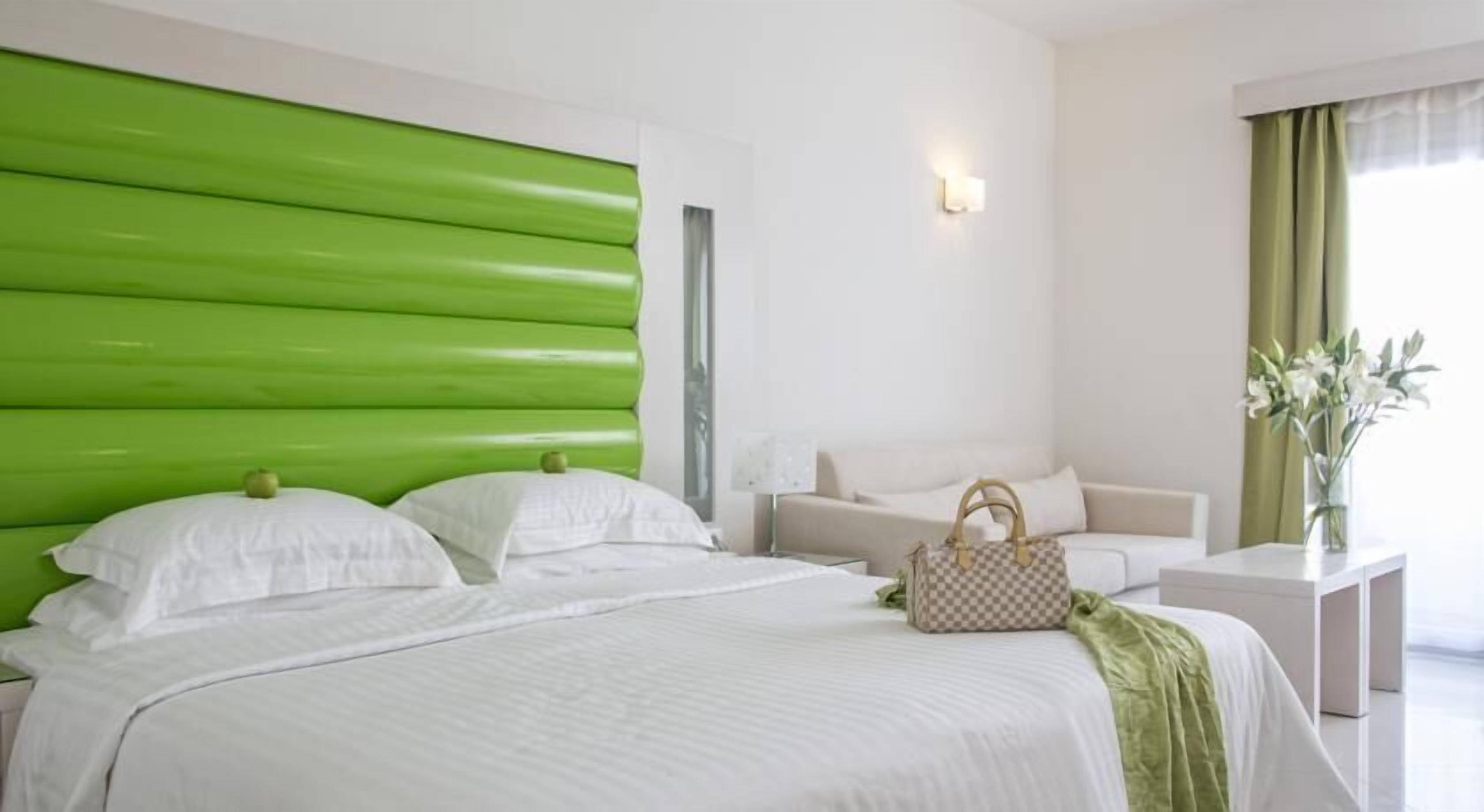 A hotel room with a large bed, a green headboard, a sofa, a nightstand, and a vase with flowers.