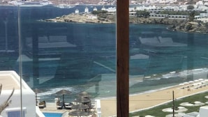 Un área de estar con paredes de vidrio y vista a una playa y un paisaje montañoso.