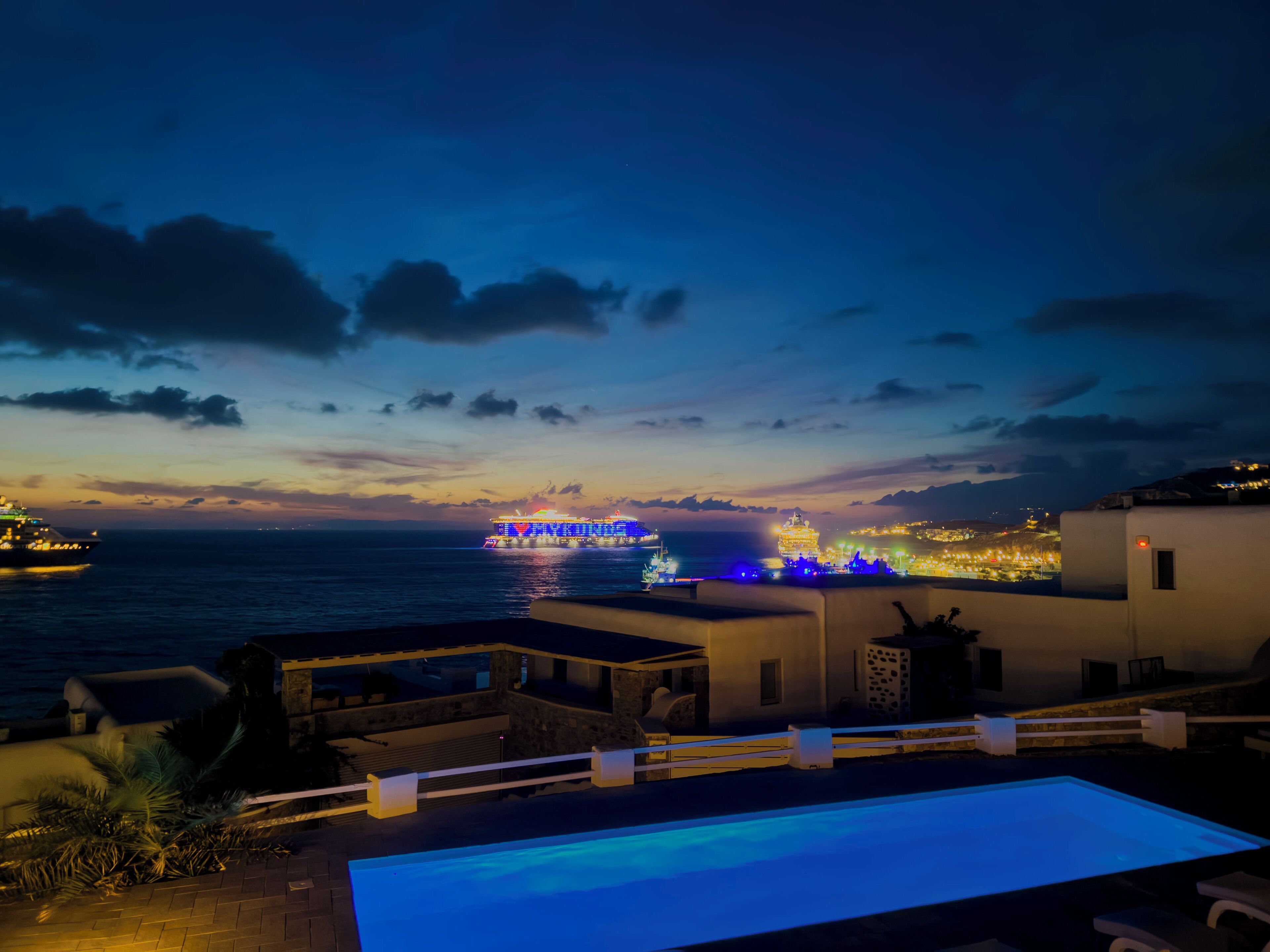 A pool area with a view of the sea and a distant illuminated ship.