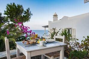 A table set with breakfast items, including bread, fruit, and a cup, overlooking a coastal view.
