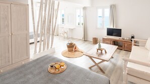 A bright, spacious room with a bed, a TV, a dining table with breakfast, and large windows offering a view. -  With-inn Mykonos Suites (Mykonos)