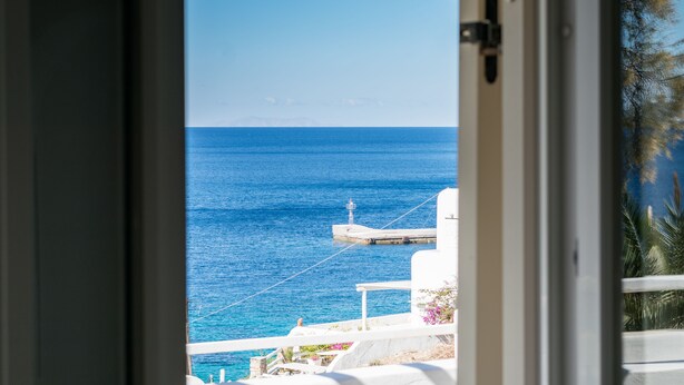 A view from a balcony overlooking a clear blue sea with a pier and white buildings. -  With-inn Mykonos Suites (Mykonos)