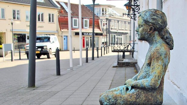 Una estatua de una figura sentada en un banco de piedra en un entorno urbano.