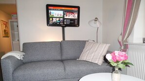 Una sala de estar con un sofá gris, una mesa blanca y un televisor de pantalla plana montado en la pared.