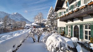 A snow-covered pathway leading to a building with traditional architecture, a mountain backdrop, and a clear sky. - Hotel Aschenbrenner (Garmisch-Partenkirchen)
