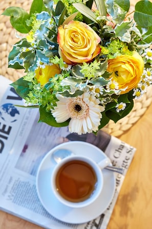 A bouquet of yellow and white flowers, a cup of tea, and a newspaper on a wooden surface. - Hotel Aschenbrenner (Garmisch-Partenkirchen)