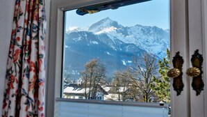 A window with a view of snow-covered mountains and a house in the foreground. - Hotel Aschenbrenner (Garmisch-Partenkirchen)