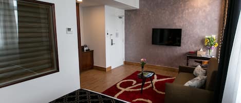 Et hotelværelse med en seng, et fjernsyn ophængt på væggen, et lille bord med en vase og en sofa.