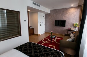 Et hotelværelse med en seng, et fjernsyn ophængt på væggen, et lille bord med en vase og en sofa.
