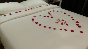 A hotel room with a neatly made bed, a bedside phone, and a power outlet on the wall.