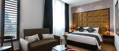 Une chambre d’hôtel moderne avec un canapé, une petite table, un lit avec une tête de lit et un tapis rouge.