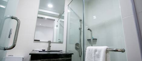 A modern bathroom with a glass shower enclosure, a sink with a black countertop, and a white towel on a towel rack.