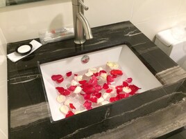 A bathroom sink with black marble countertop, a silver faucet, and rose petals in the water.
