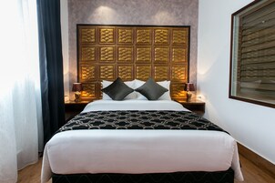 A neatly made bed with a patterned bedspread, a headboard with a geometric design, and bedside lamps.