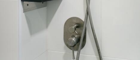Ducha con cabezal de ducha y manguera de mano, montados en una pared con azulejos blancos.