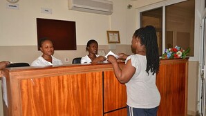 A reception area with a wooden reception desk, a clock, and a framed certificate on the wall. - Kunta Kinte Hotel (Accra)