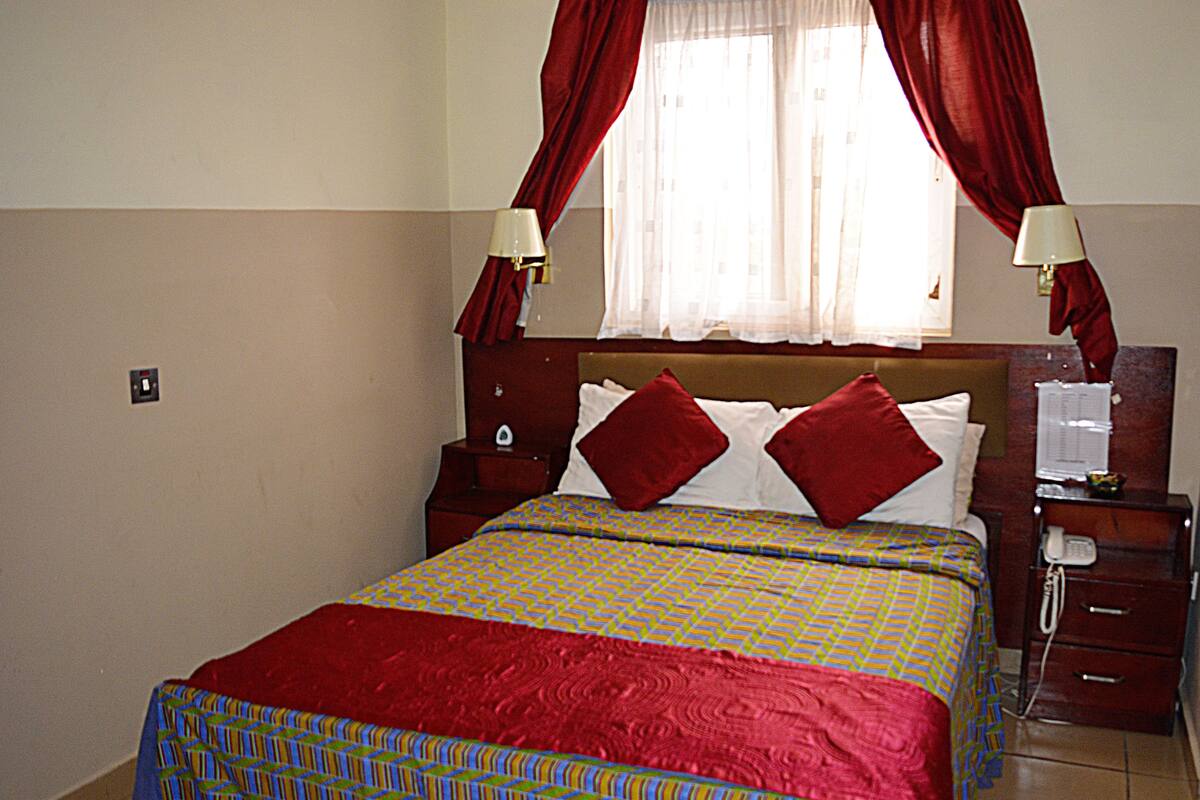 A hotel room with a bed, a nightstand, a telephone, and a window with curtains.