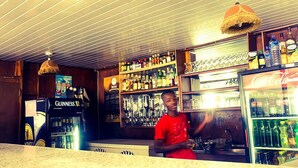 A bar area with shelves stocked with various bottles, a Guinness refrigerator, and a Coca-Cola cooler. - Kunta Kinte Hotel (Accra)