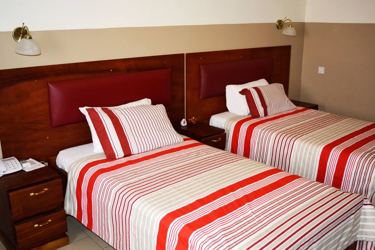 A hotel room with two beds, each with a wooden headboard, red and white striped bedding, and bedside tables with lamps.