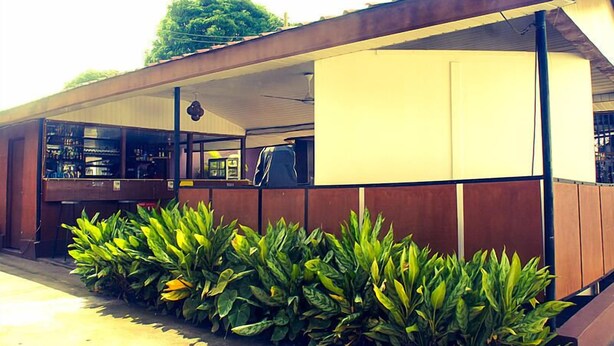 A building with a covered outdoor area, a counter with items on display, and a row of plants in front. - Kunta Kinte Hotel (Accra)
