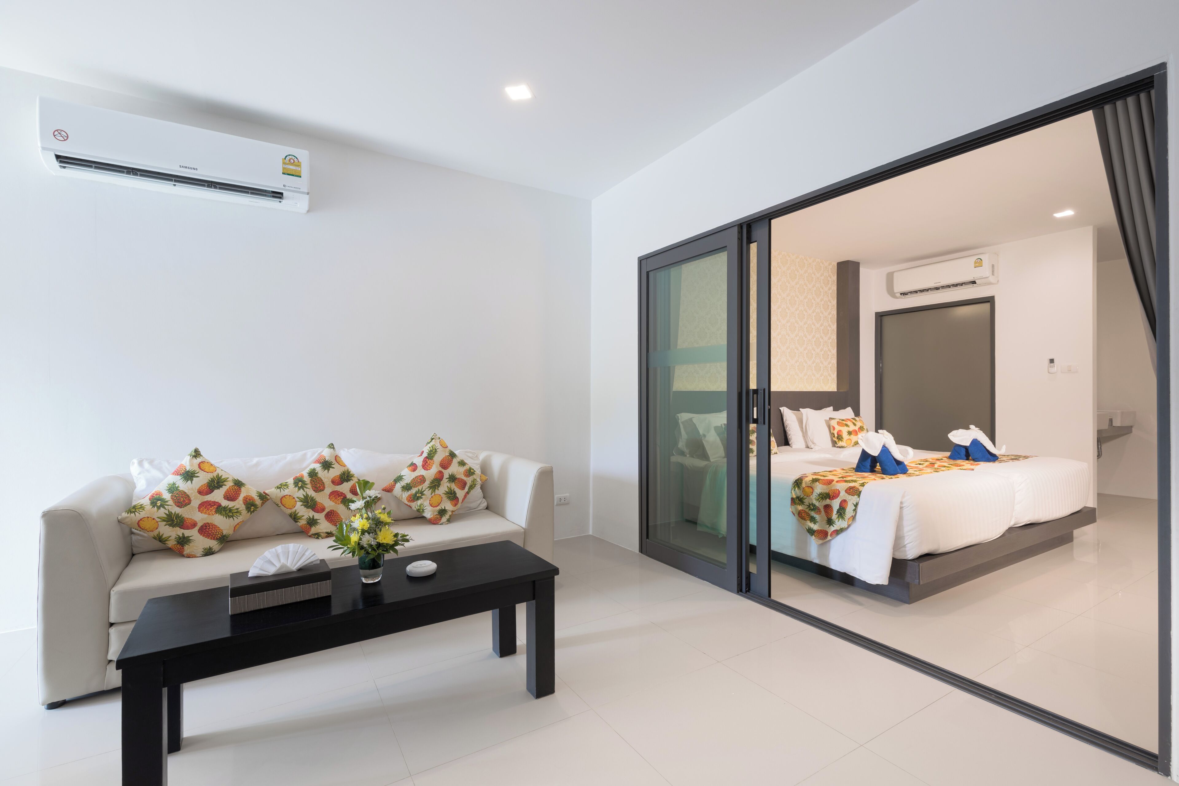 A modern hotel room with a sofa, a coffee table, and a bed with a white bedspread.