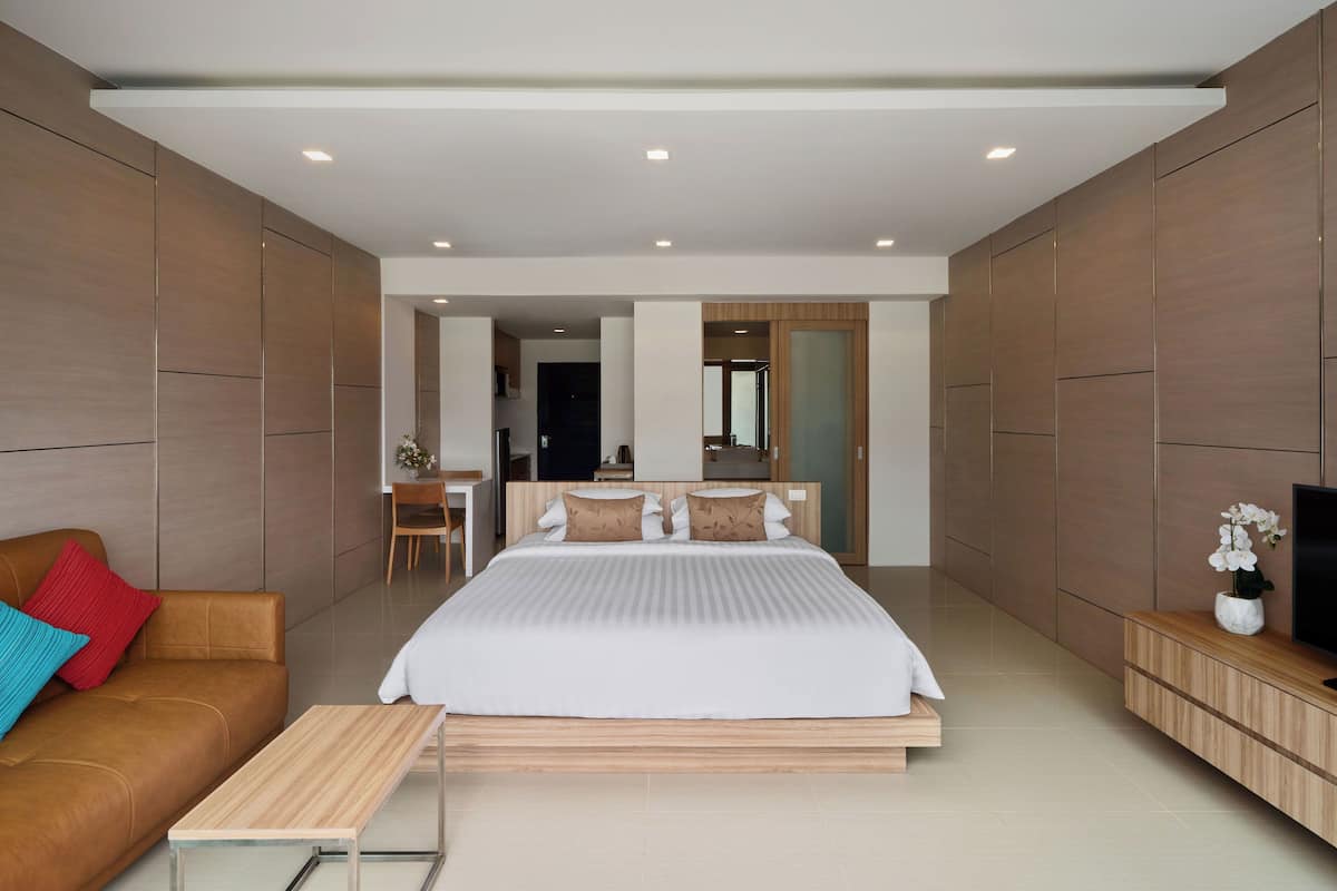A modern hotel room with a large bed, a wooden bench, a TV, and a desk with a chair.