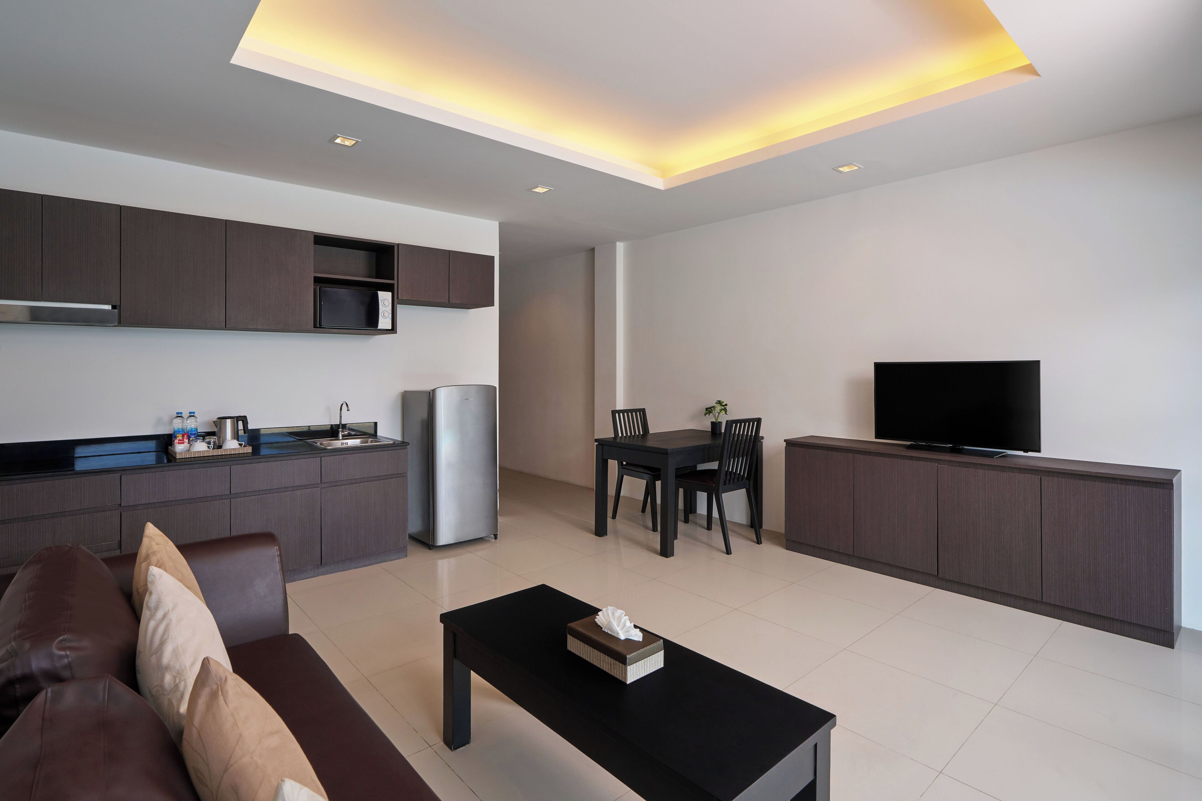 Una sala moderna con un sofá, una mesa de centro, una zona de comedor con mesa y sillas, una cocina con armarios y electrodomésticos, y un televisor montado en la pared.
