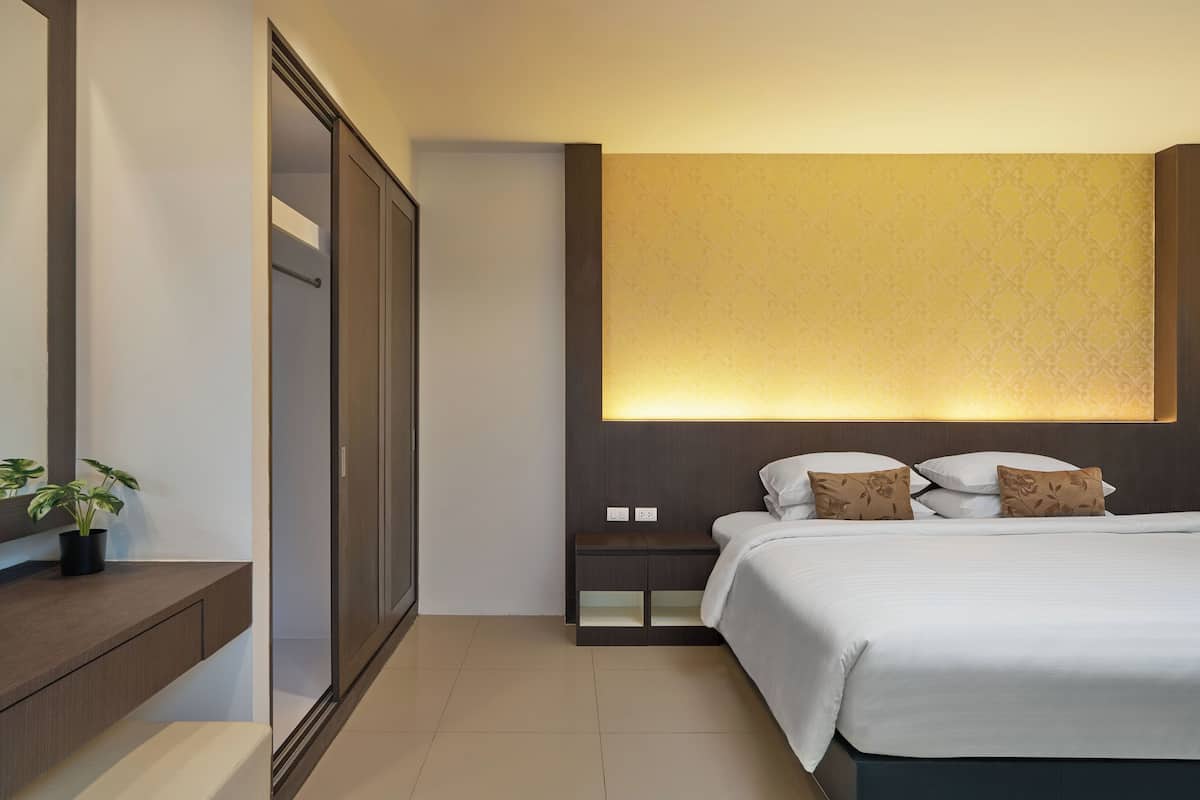A modern hotel room with a large bed, a nightstand, a wardrobe, and a wall-mounted light fixture.