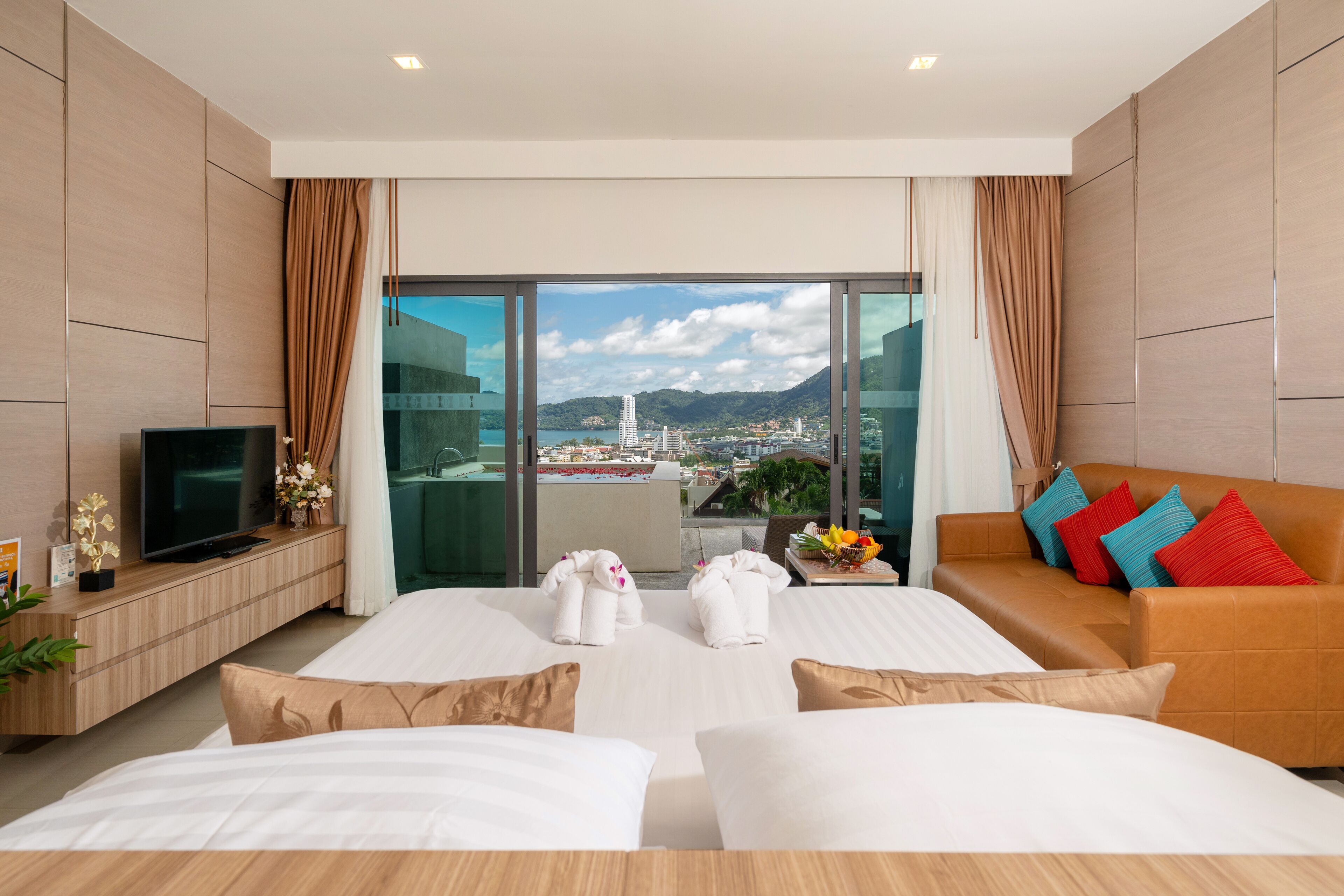 Una habitación de hotel moderna con una cama grande, un sofá, un televisor y un balcón con vista a la ciudad.