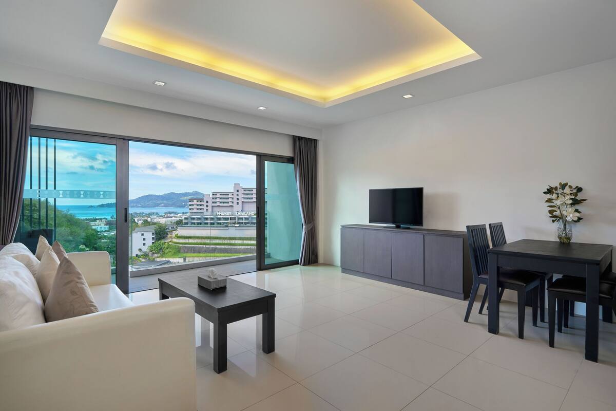 A modern living room with a sofa, a dining table with chairs, a TV, and a view of the cityscape.