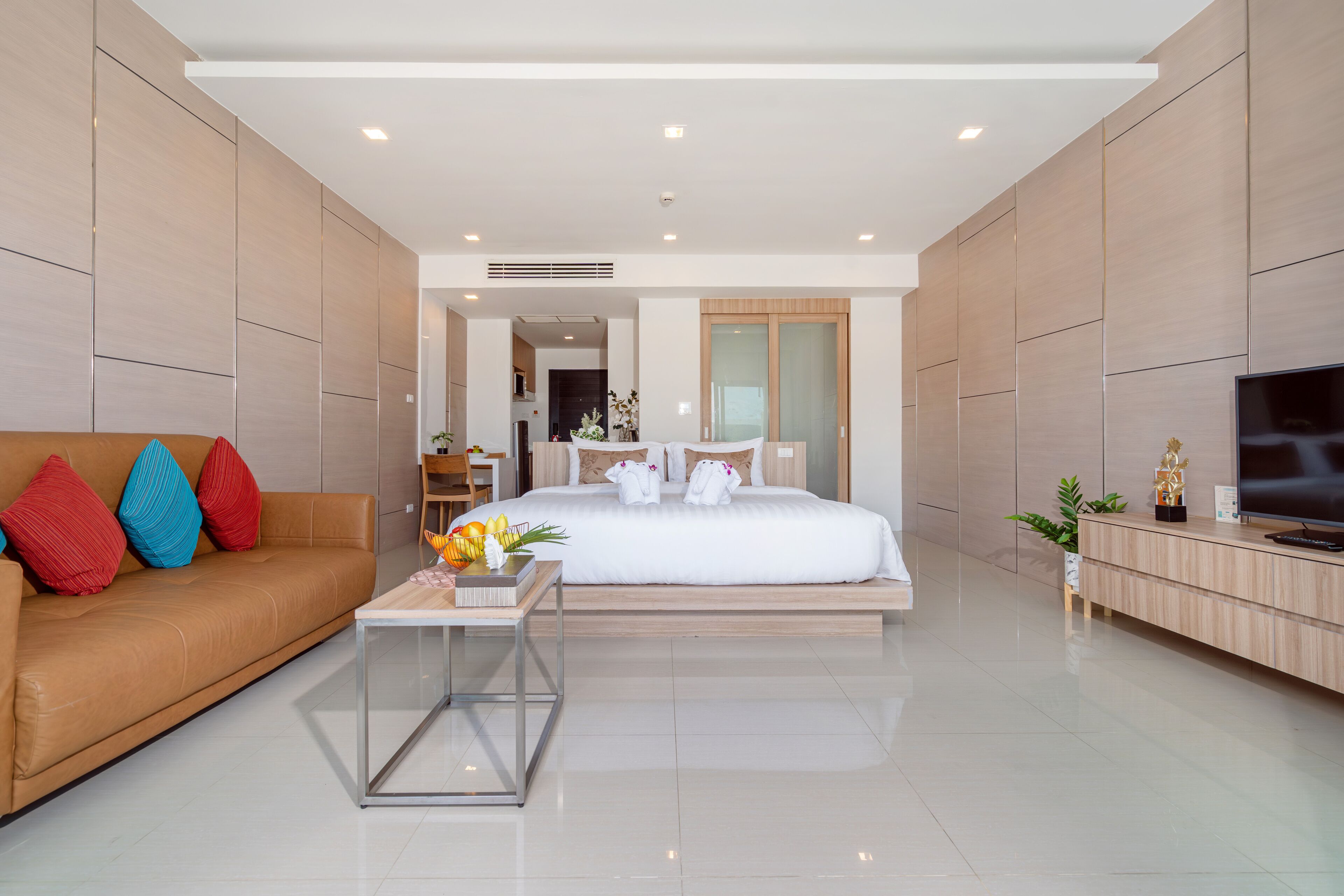 A modern hotel room with a large bed, a sofa, a TV, and a small table with flowers.