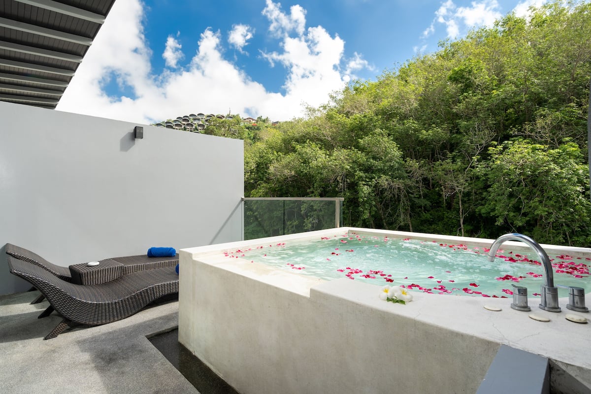 A spa area with a hot tub surrounded by greenery, a lounge chair, and a modern architectural design.