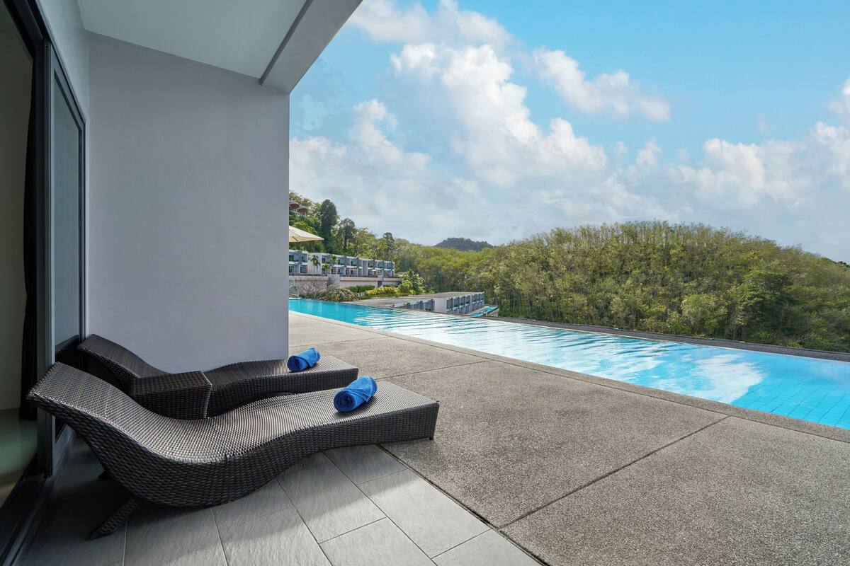 A poolside area with two wicker lounge chairs and a pool.