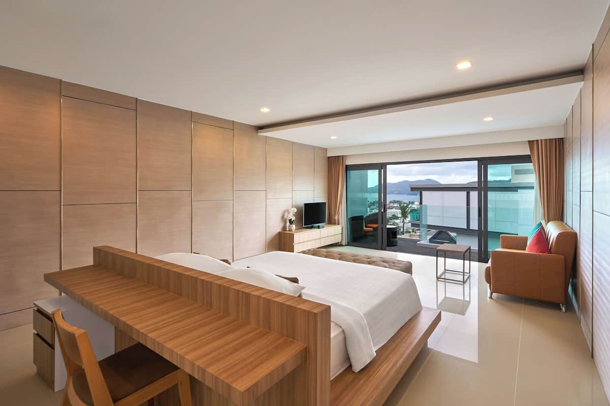 A modern hotel room with a large bed, a wooden desk, a TV, and a balcony with a view of the mountains.