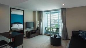 A modern hotel room with a bed, a TV, a desk with a chair, a coffee table, and a large window with curtains. - Silom Lofts Hotel (Bangkok)