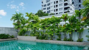 Una piscina con diseño de cuadros, rodeada de palmeras y un edificio moderno al fondo.