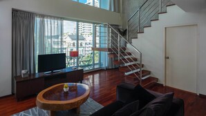 A spacious living area with a large window, a staircase, and a flat-screen TV. - Silom Lofts Hotel (Bangkok)