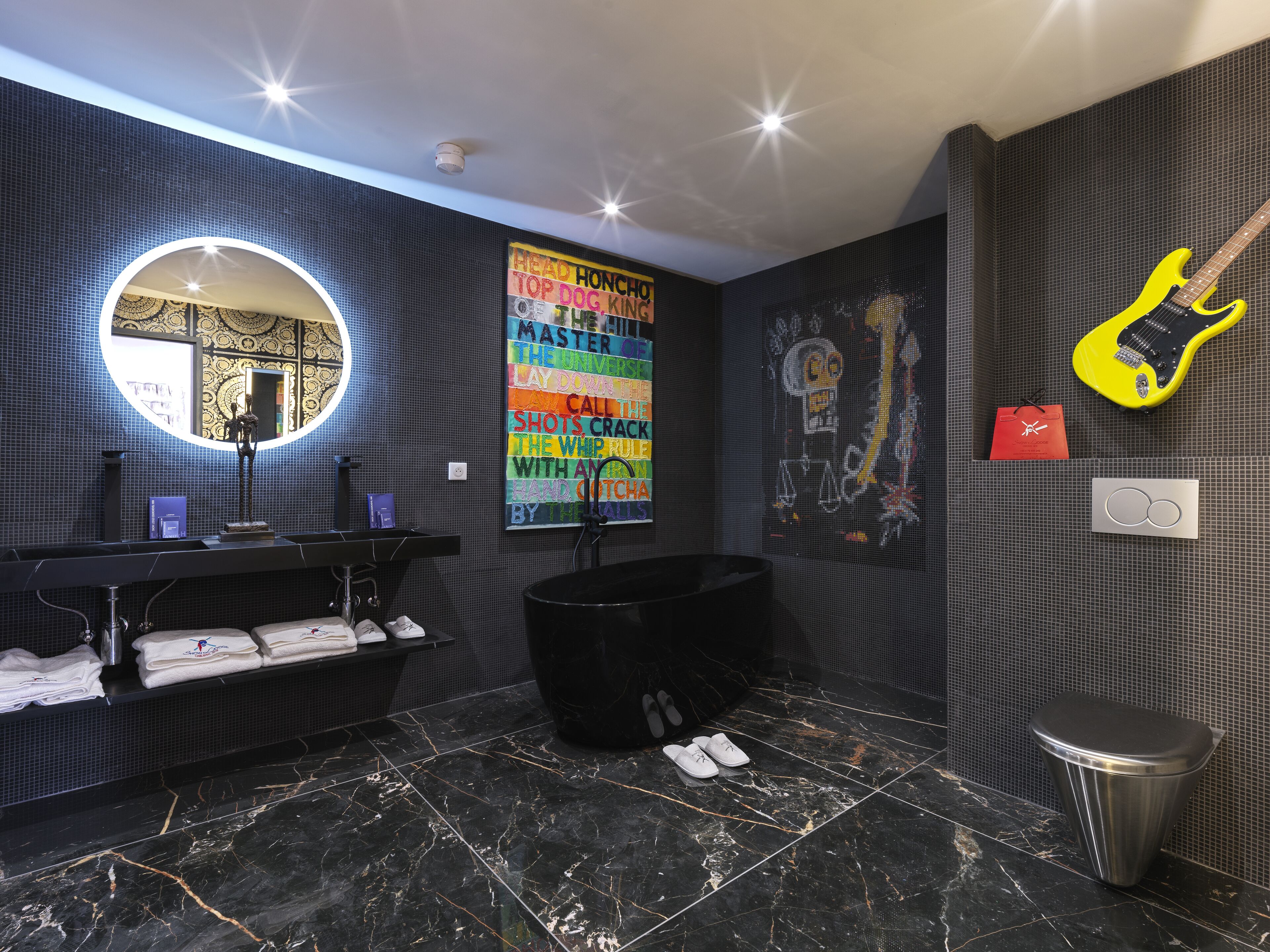 A modern bathroom with a black bathtub, a round mirror, and a colorful poster on the wall.