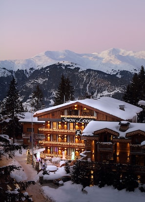 Eine Schneelodge mit einem Schild, auf dem "Snow Lodge" steht, und Blick auf verschneite Berge im Hintergrund.