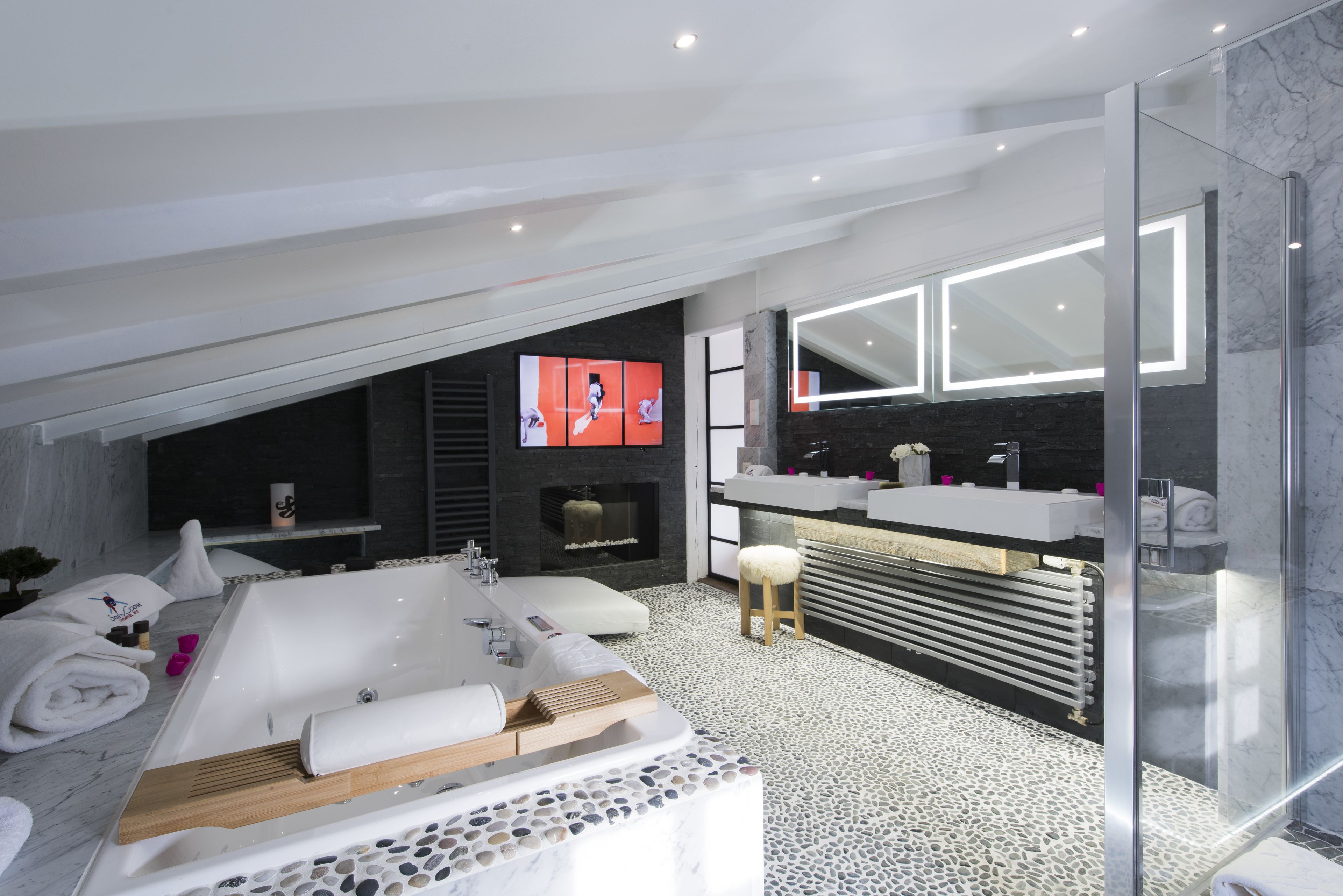 A modern bathroom with a freestanding bathtub, a large mirror, and a television mounted on the wall.