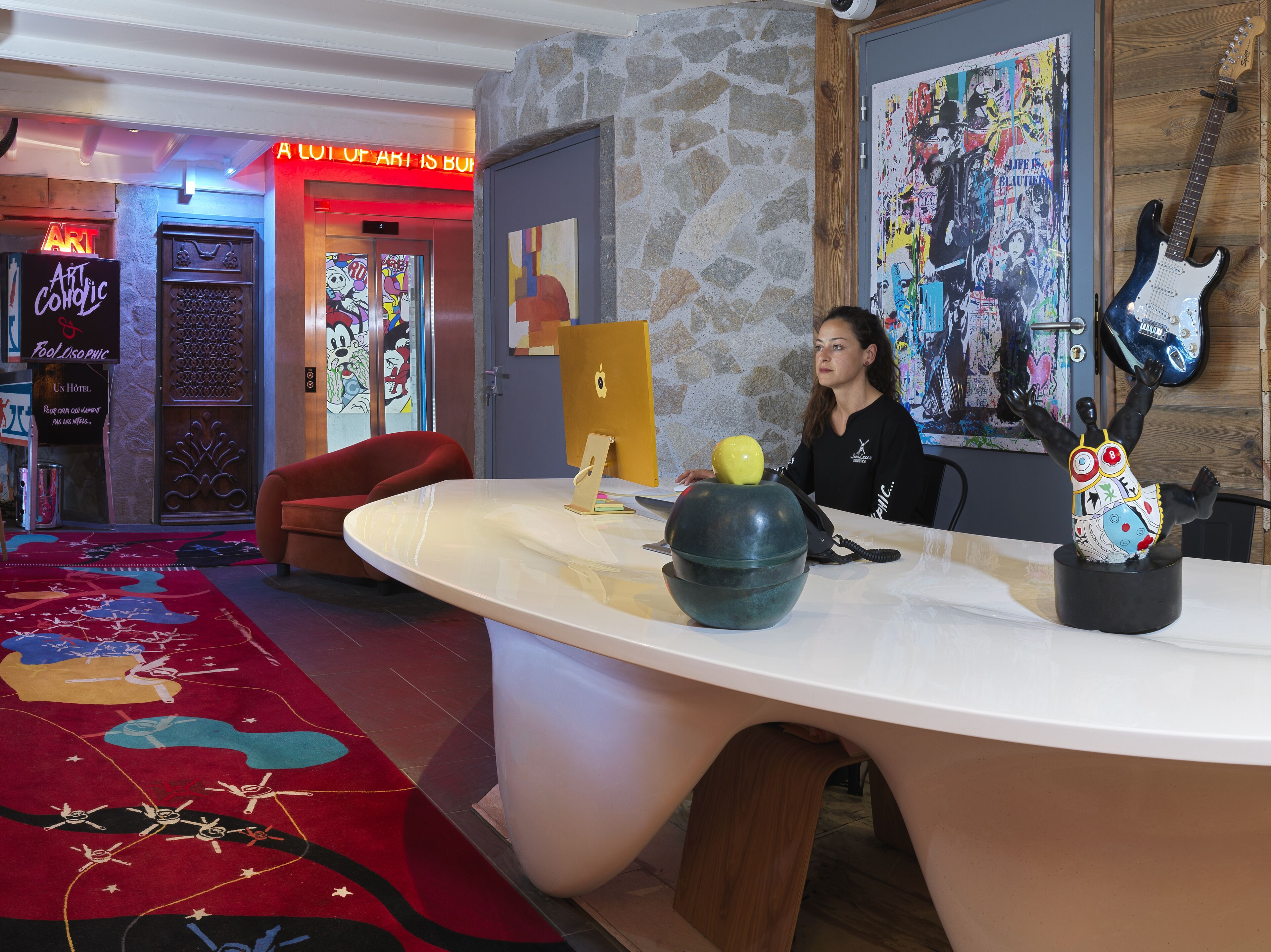 A hotel lobby with a large reception desk, a red armchair, and a colorful carpet.