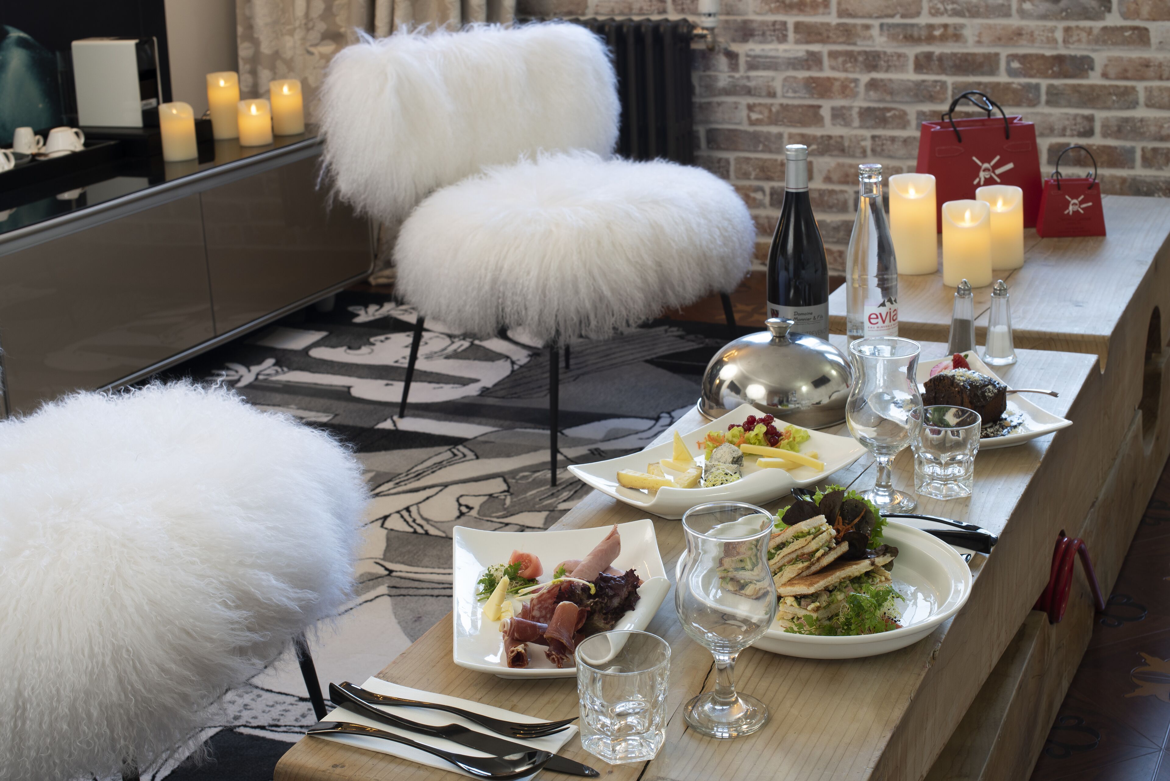 A dining table set with plates of food, glasses, candles, and a bottle of wine.