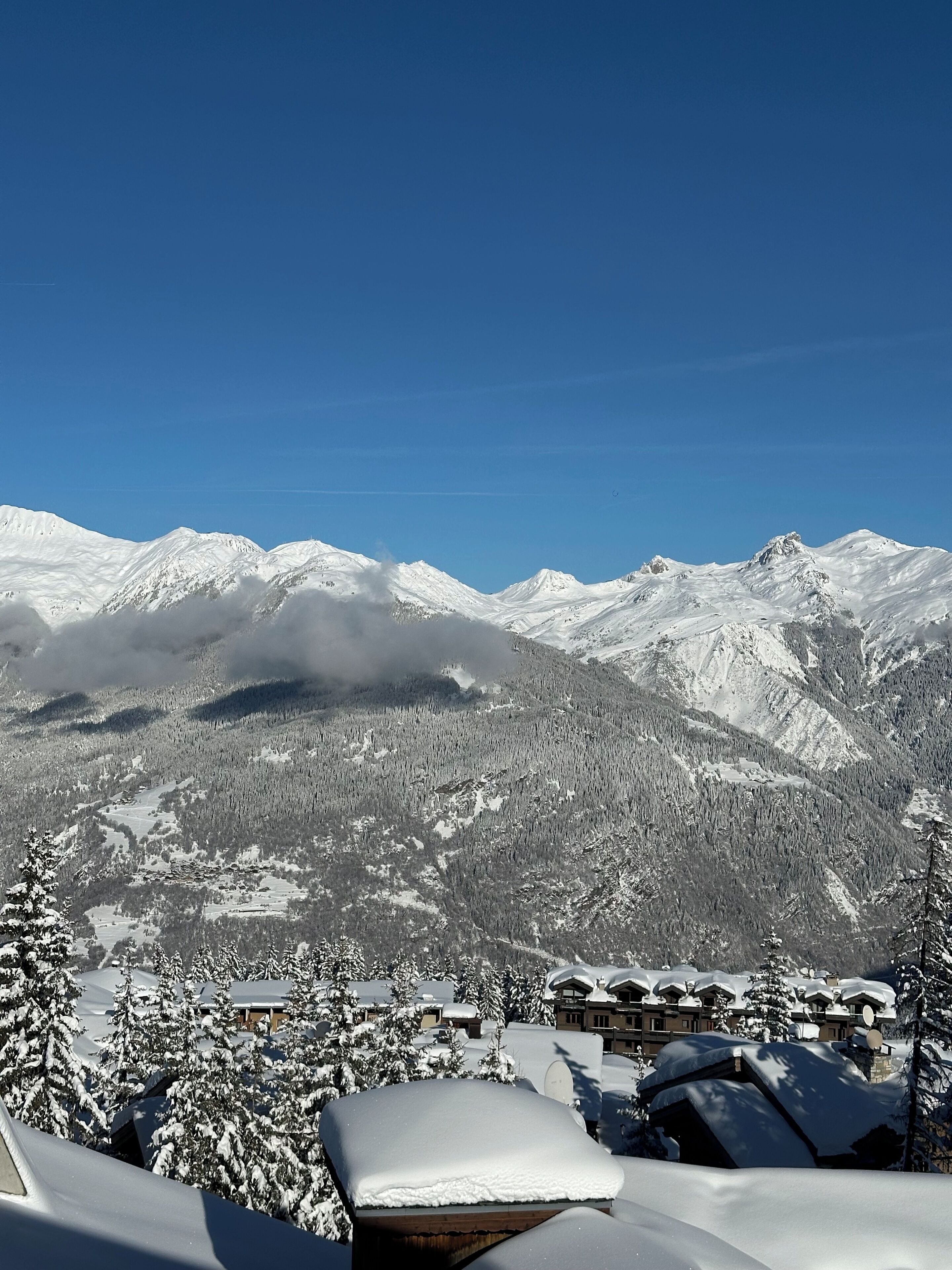 A snow-covered mountain landscape with a resort area in the foreground, featuring snow-covered roofs and buildings.