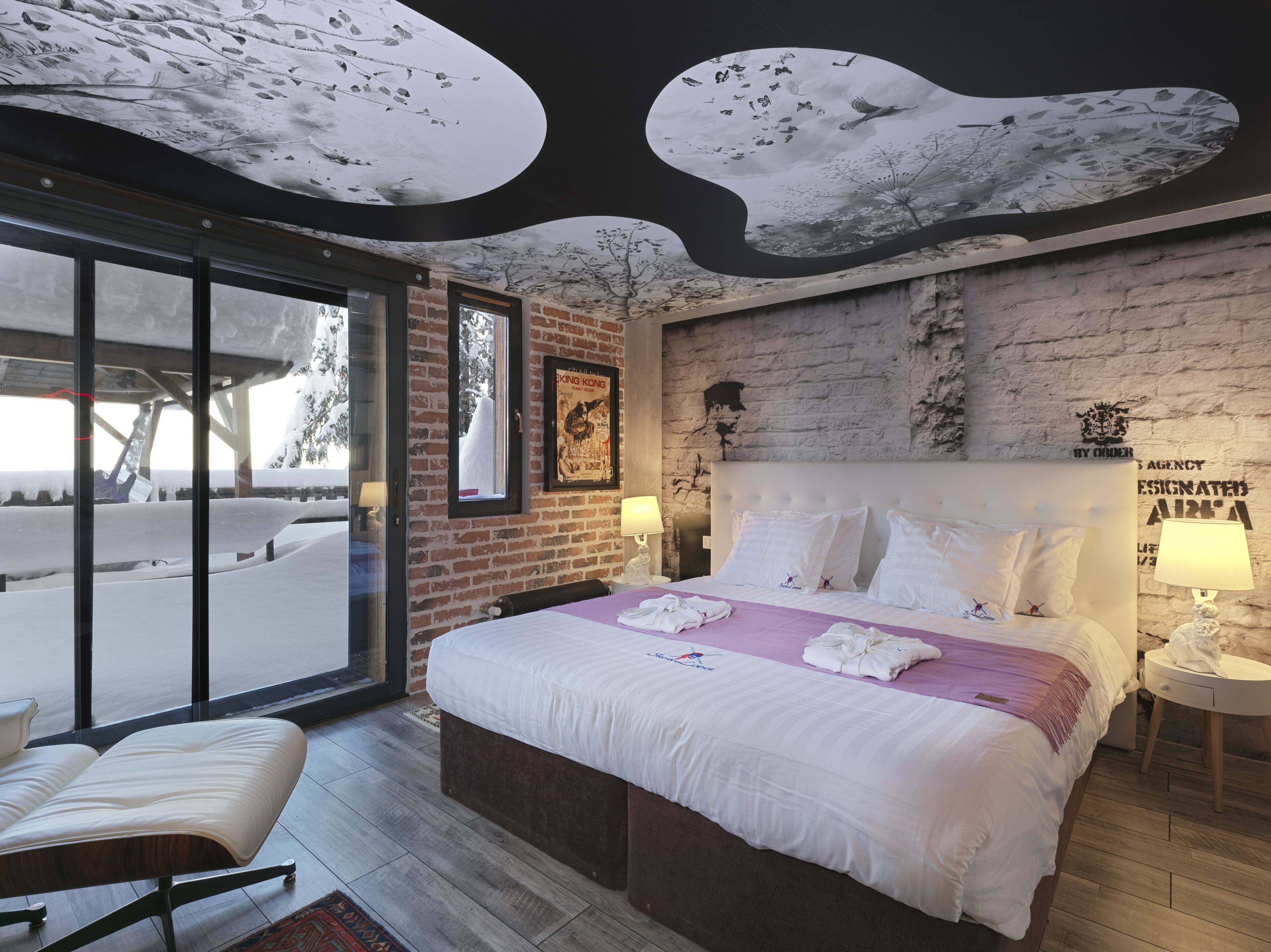 Habitación de hotel con una cama grande, ventana, pared de ladrillo y un techo de diseño único.
