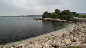 A rocky shoreline with clear water, a boat in the distance, and a road curving along the coast. - Galaxy Hotel (Kefalonia)