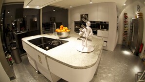 Una cocina moderna con una isla central, un fregadero y una estufa. Hay un bol con naranjas sobre la isla y una escultura blanca.